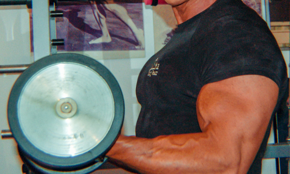 Bodybuilder in palestra solleva un bilanciere, mostrando i bicipiti scolpiti e muscoli in tensione.